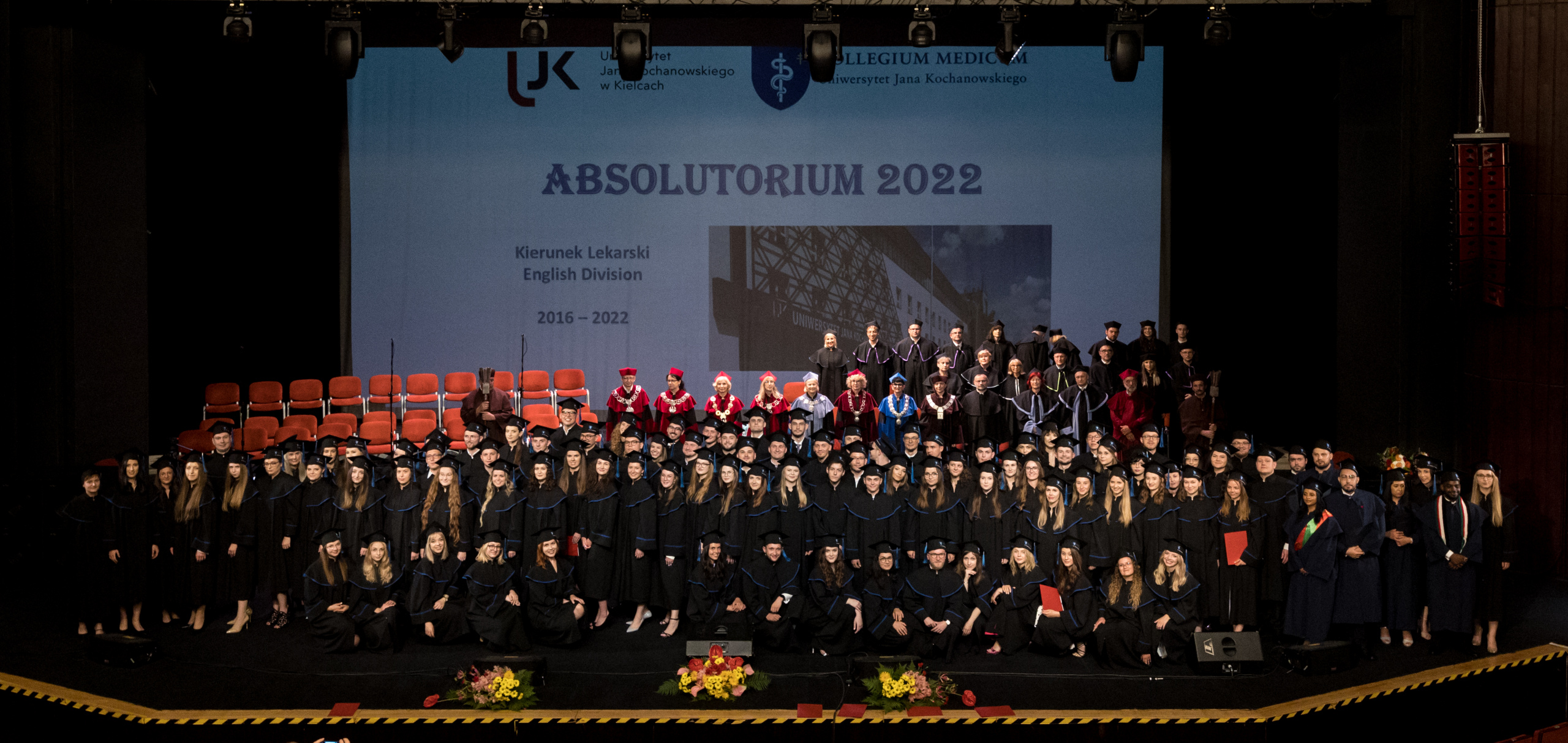 Zbiorowe zdjęcie absolwentów, władz i przedstawicieli Senatu uczelni. Wszyscy stoją na scenie.