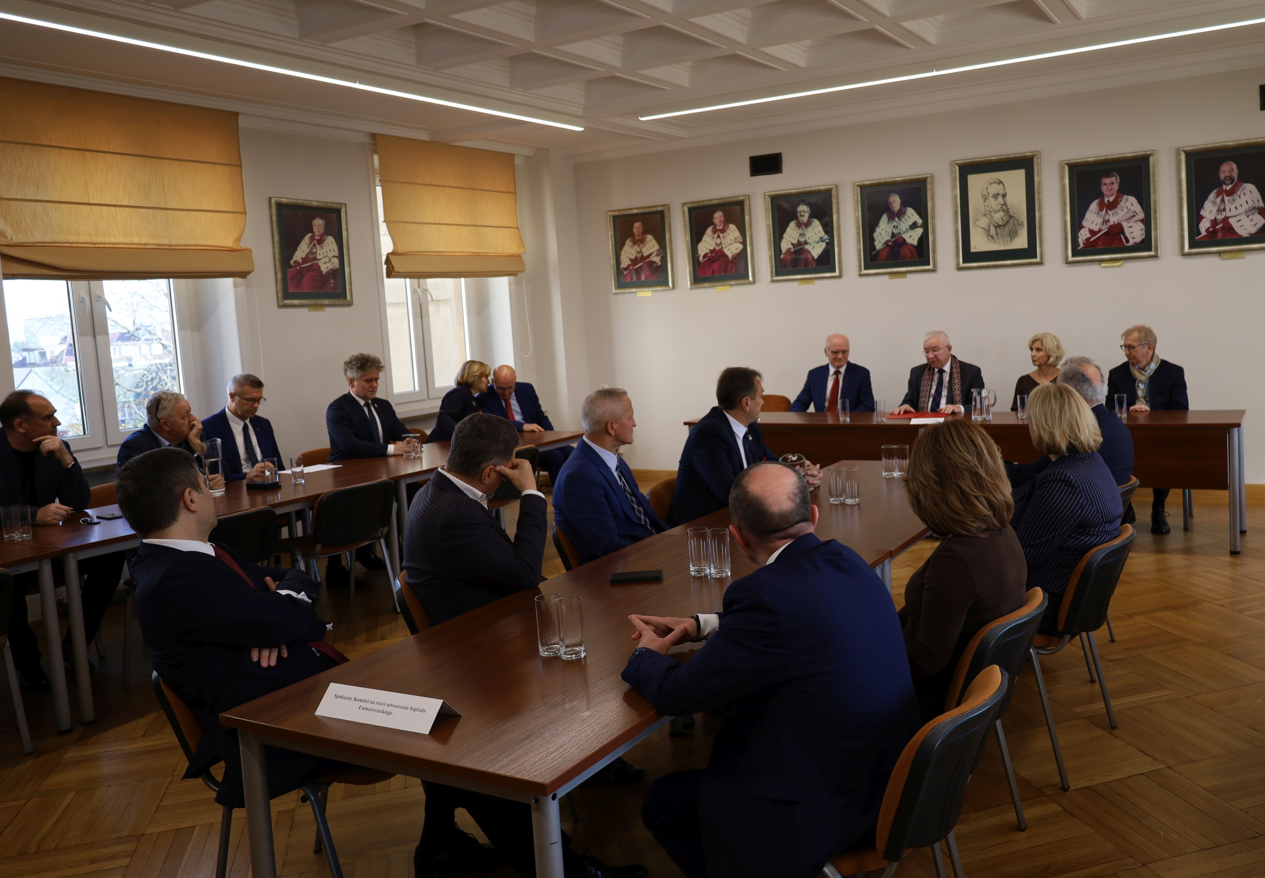 Uczestnicy spotkania w sali Rektoratu. W tle prezydium i poczet rektorów Uczelni.