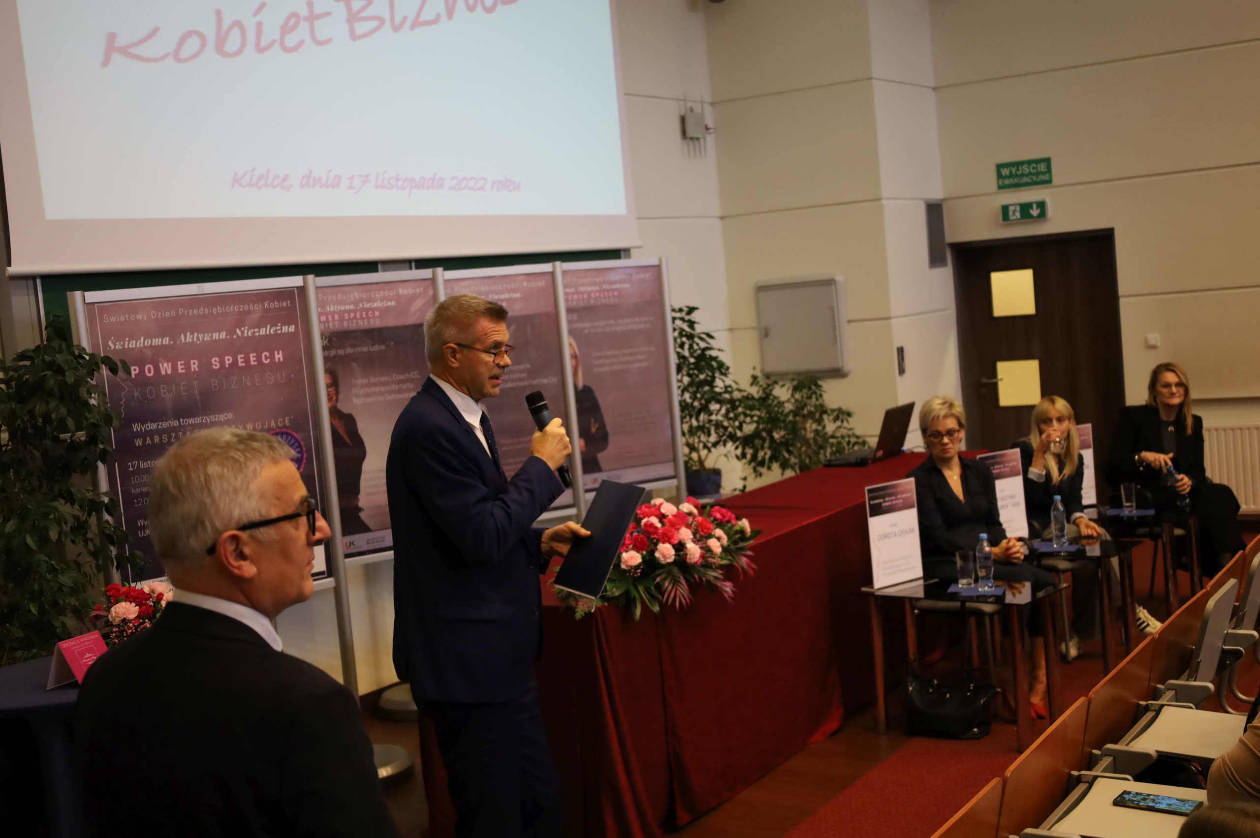 Przy mikrofonie Bogdan Wenta, prezydent Kielc. W tle kompozycje kwiatów.
