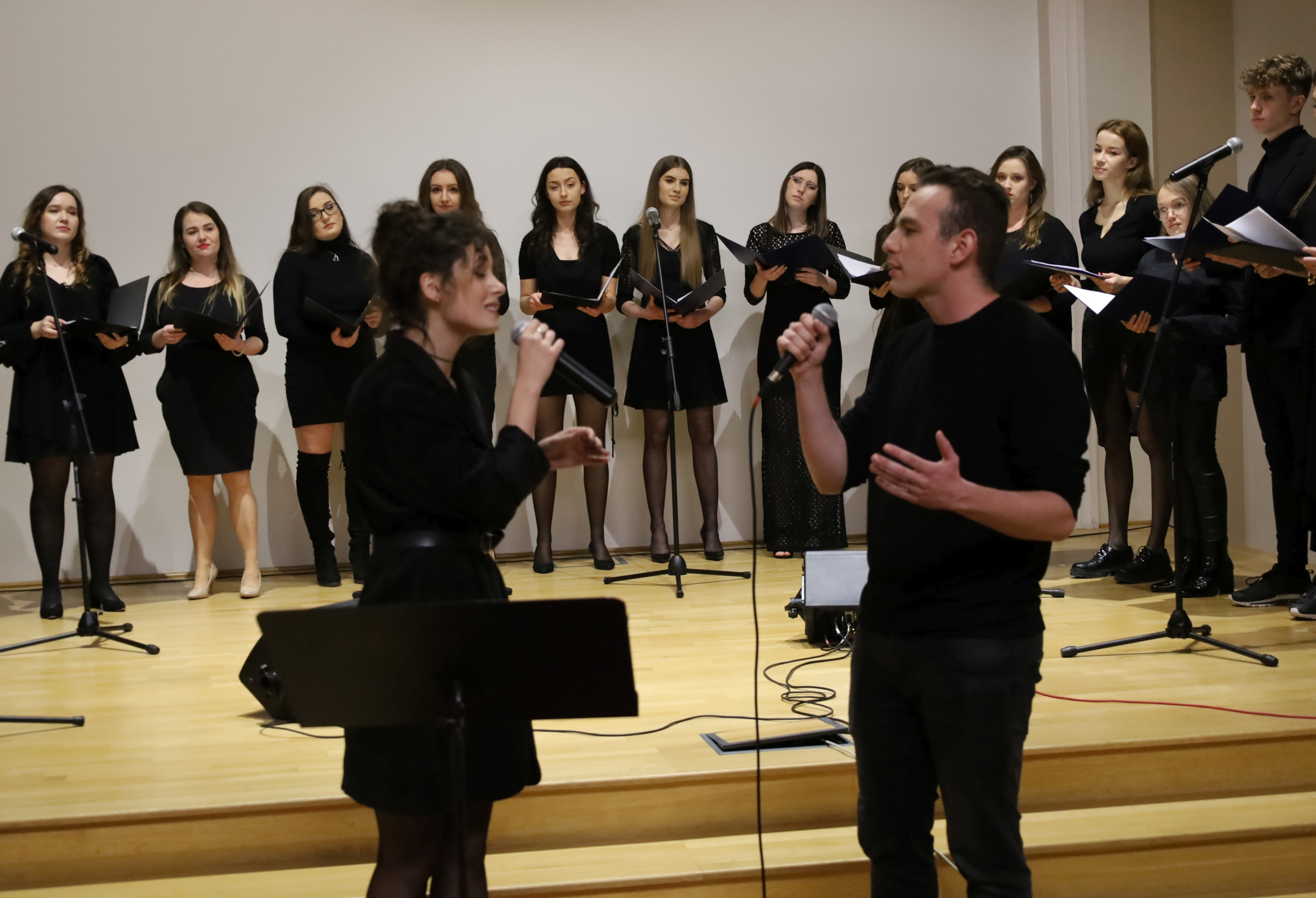 Duet studentów przy mikrofonie, w tle chór złożony z pozostałych studentów UJK.