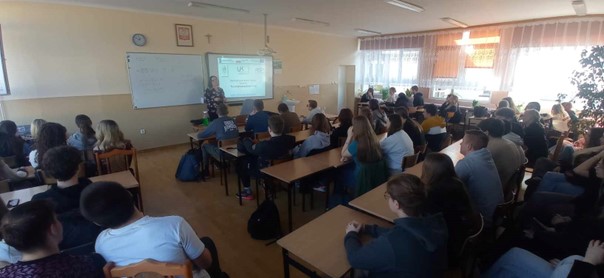 Przedstawicielka kadry UJK prezentuje w jednej ze szkół zakres wsparcia w ramach projektu. W klasie siedzą uczniowie w ławkach. Jest ich bardzo dużo.