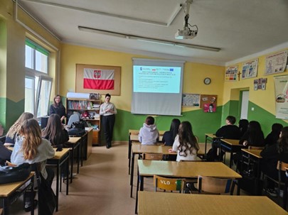 Przedstawicielki kadry UJK w Kielcach przedstawiają na prezentacji wyświetlanej w sali szkolnej ofertę kierunku Kosmetologia. Uczniowie siedzą w ławkach.