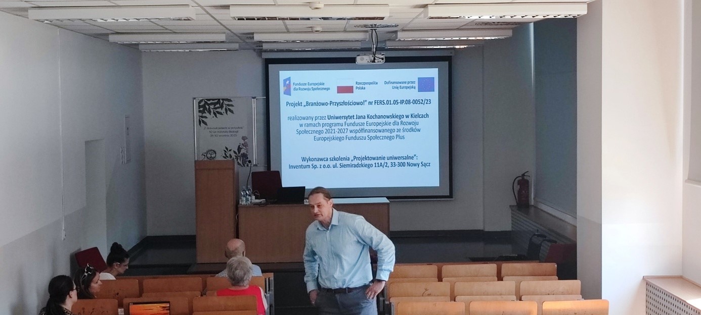 Na zdjęciu znajduje się sala wykładowa, wyświetlona prezentacja szkoleniowa oraz trener z uczestnikami
