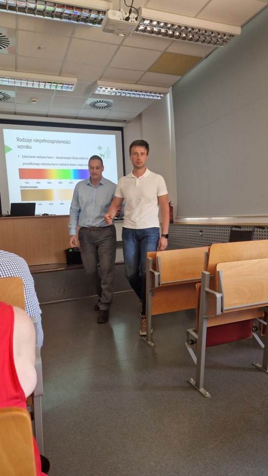 W sali szkoleniowej trener i jeden z uczestników wykonują ćwiczenie związane z rodzajami niepełnosprawności wzroku.